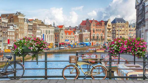 Bicycle parked on a bridge over a river with buildings in background - Amsterdam