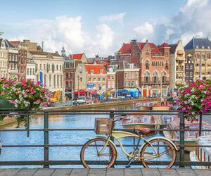 Bicycle parked on a bridge over a river with buildings in background - Amsterdam